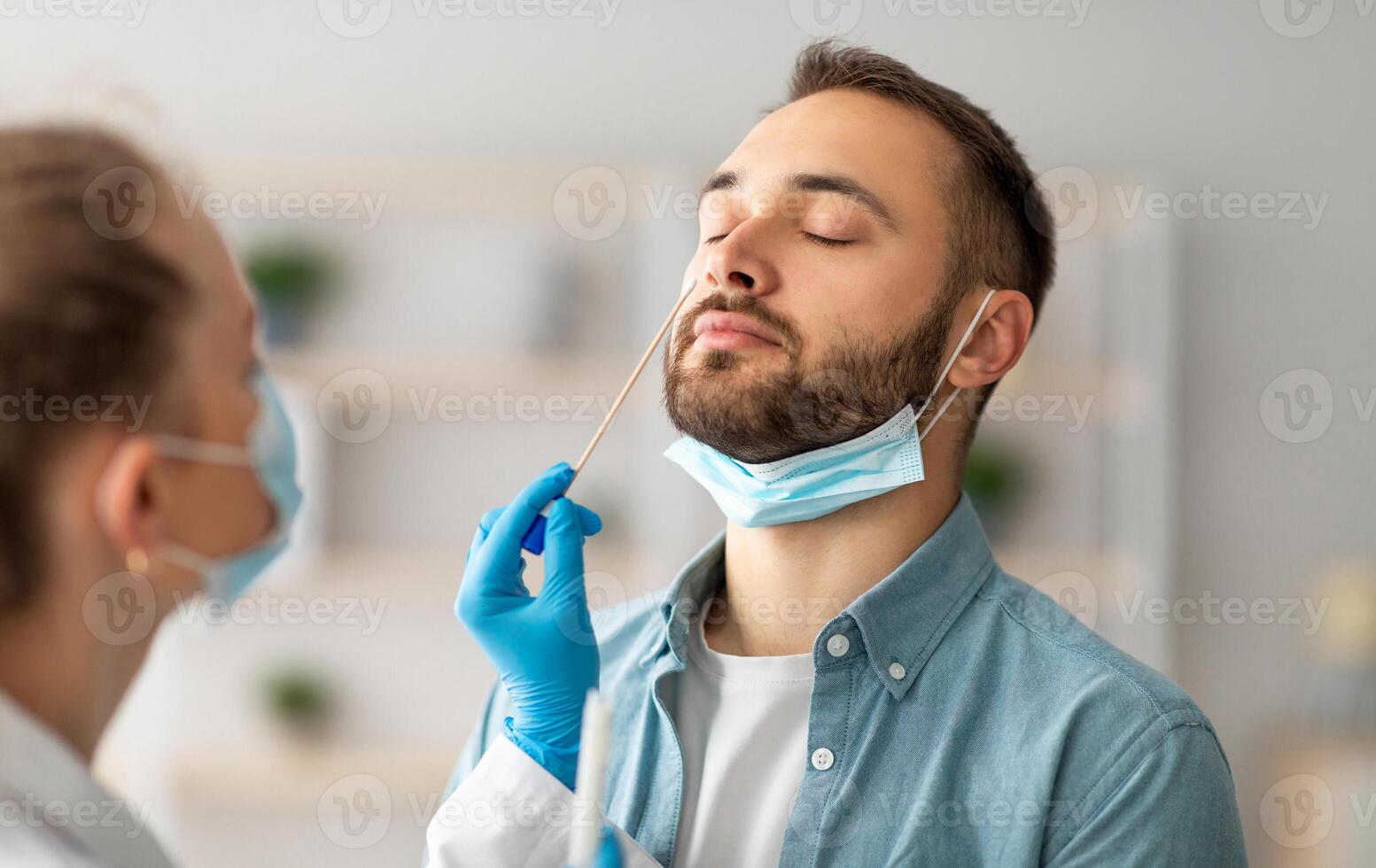 Nasal coronavirus PCR test. Doctor using swab stick to take covid virus specimen from potentially infected young guy at home. Viral disease prevention and diagnostics concept photo
