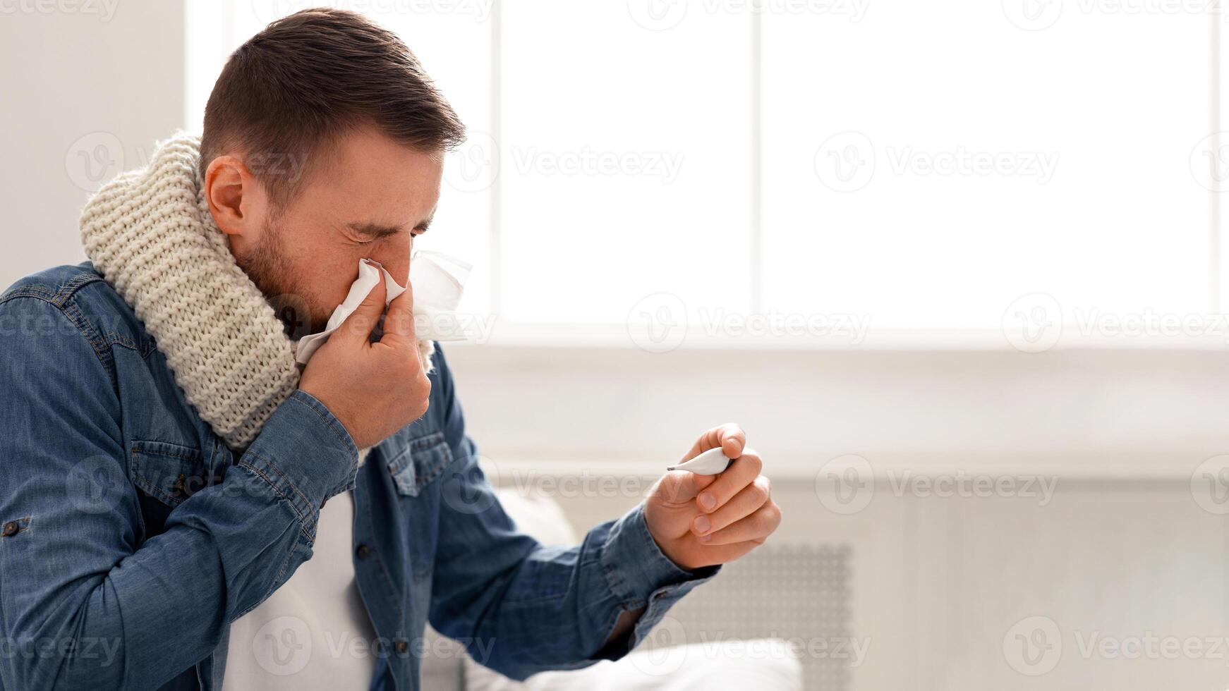 Infection symptoms. Sick man with fever blowing his runny nose at home, free space photo