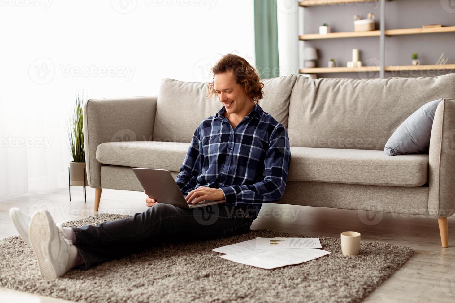 Distant Work. Happy Freelancer Man Using Laptop Working Online Sitting On Floor At Home. Relaxed Guy Browsing Internet On Computer In Living Room Indoor. Freelance, Remote Job, Internet And Technology photo