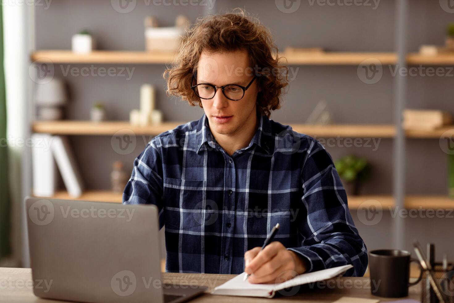 Serious Businessman At Laptop Working Taking Notes Doing Business Accounting For Report Sitting In Modern Office, Wearing Eyeglasses. Employee Worker Writing Schedule At Workplace Indoors photo