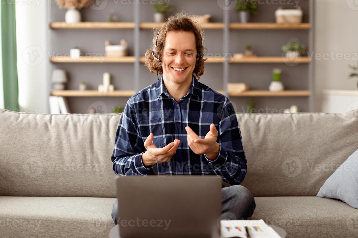Freelancer Man Using Laptop Making Call Talking To Computer Webcam Communicating Online Sitting On Couch At Home, Wearing Headset. Freelance And Technology, Distant Work And Modern Communication photo