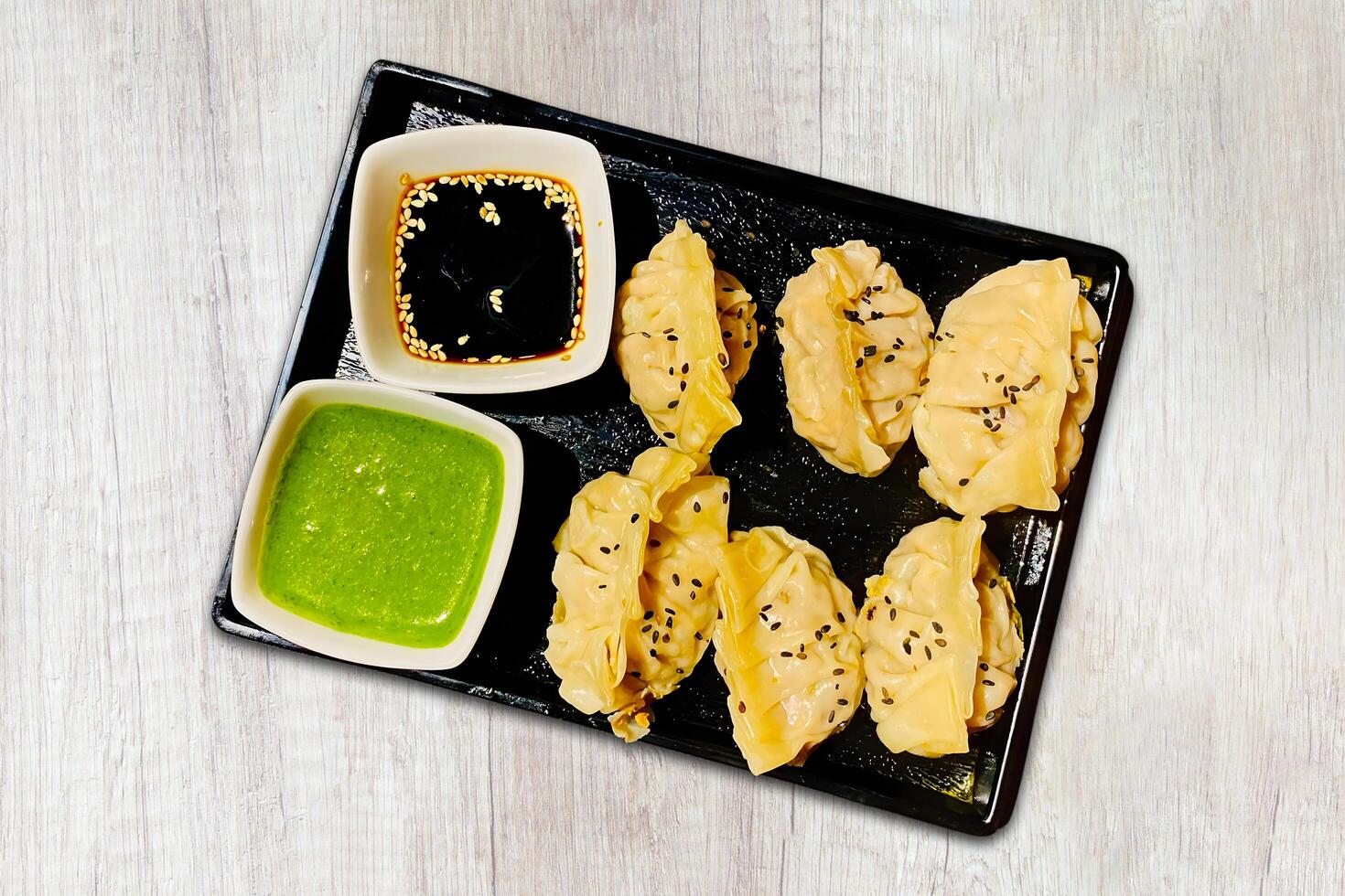 Traditional Japanese gyoza dumplings served with sauce on a black plate on a wooden background, top view photo
