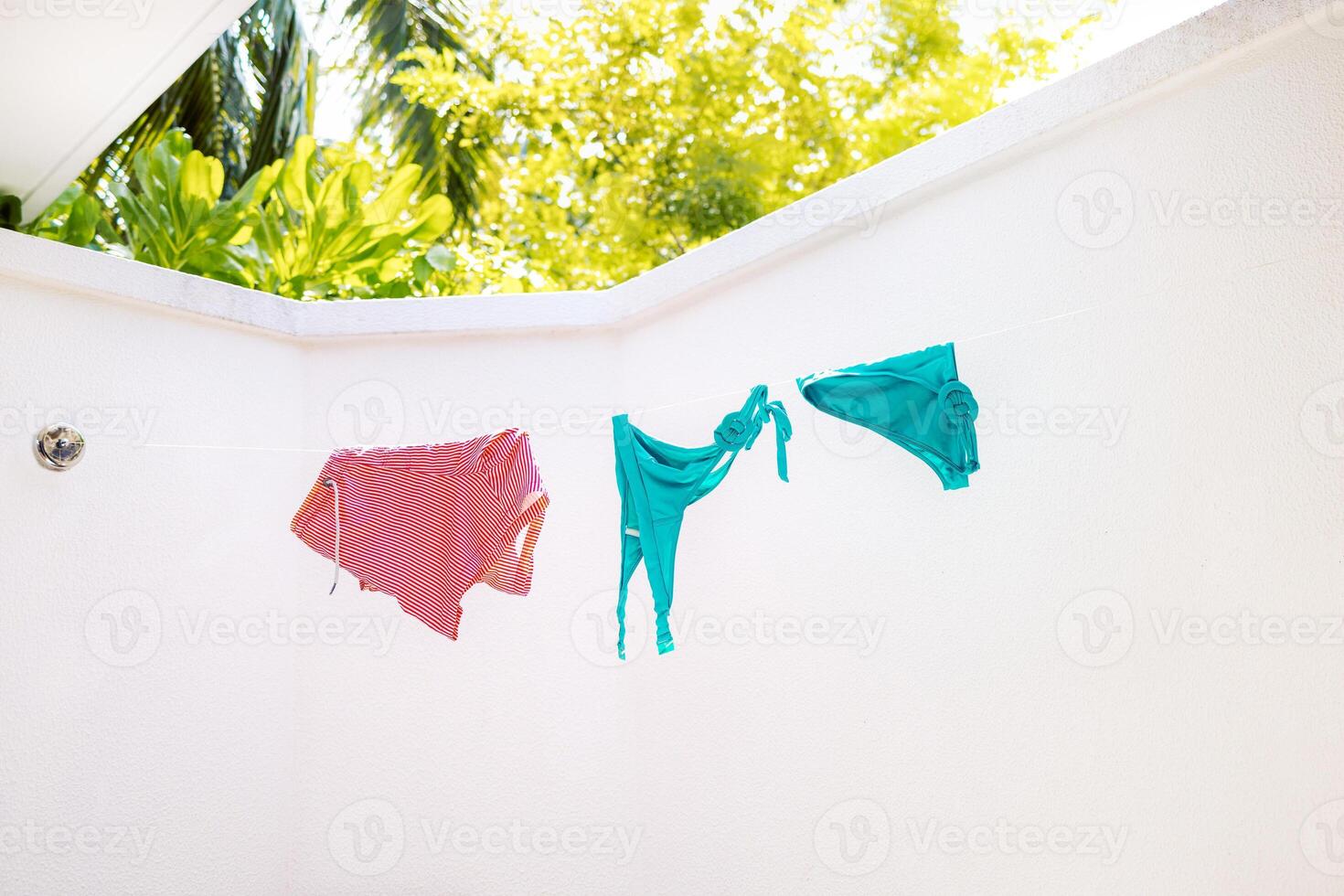 Bright swimsuits are drying outside. Wet bathing clothes are hanging on a rope. White walls and tropical plants. photo