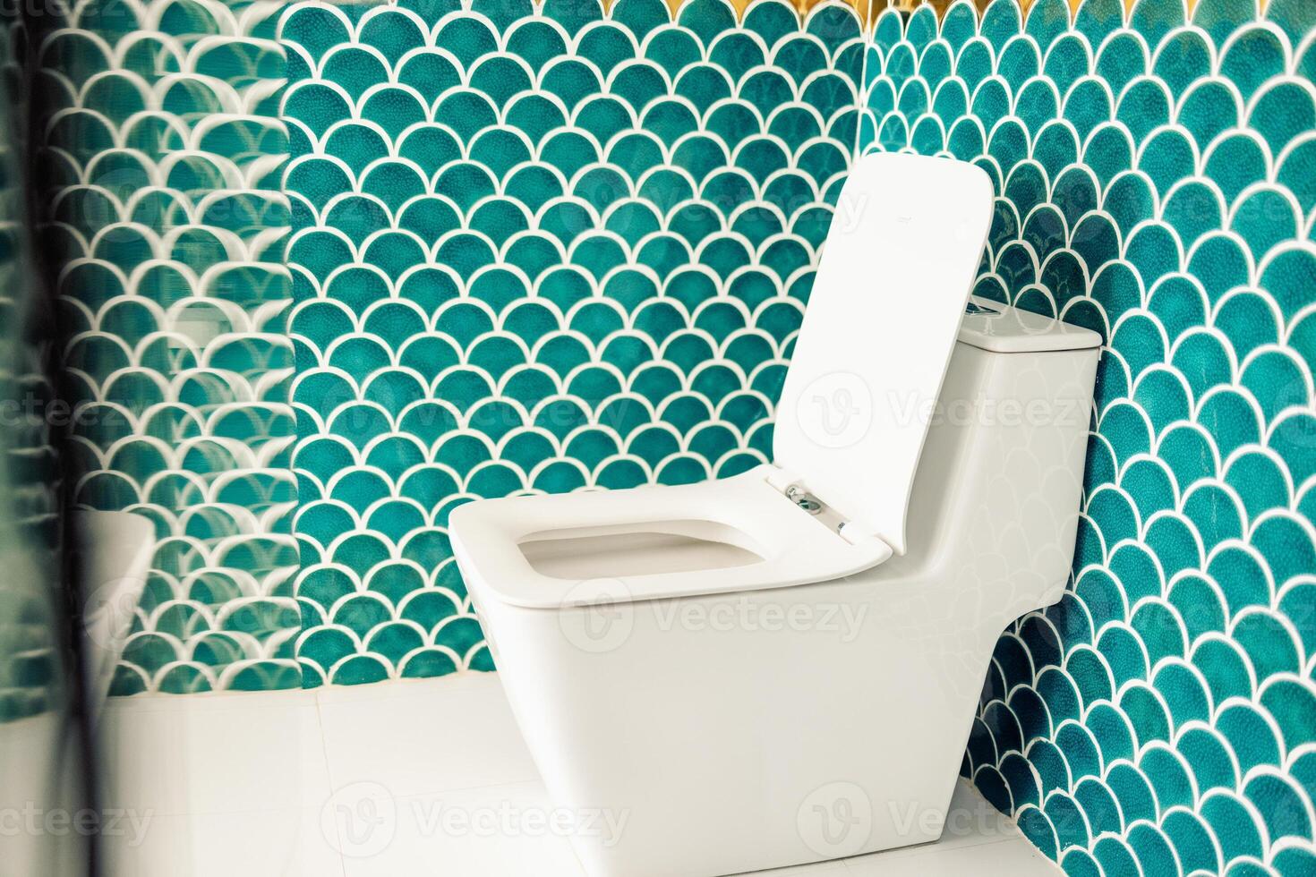 Close-up of a clean white toilet in a stylish bathroom. The modern neat room is decorated with contrasting blue and gold tiles in the form of fish scales. photo