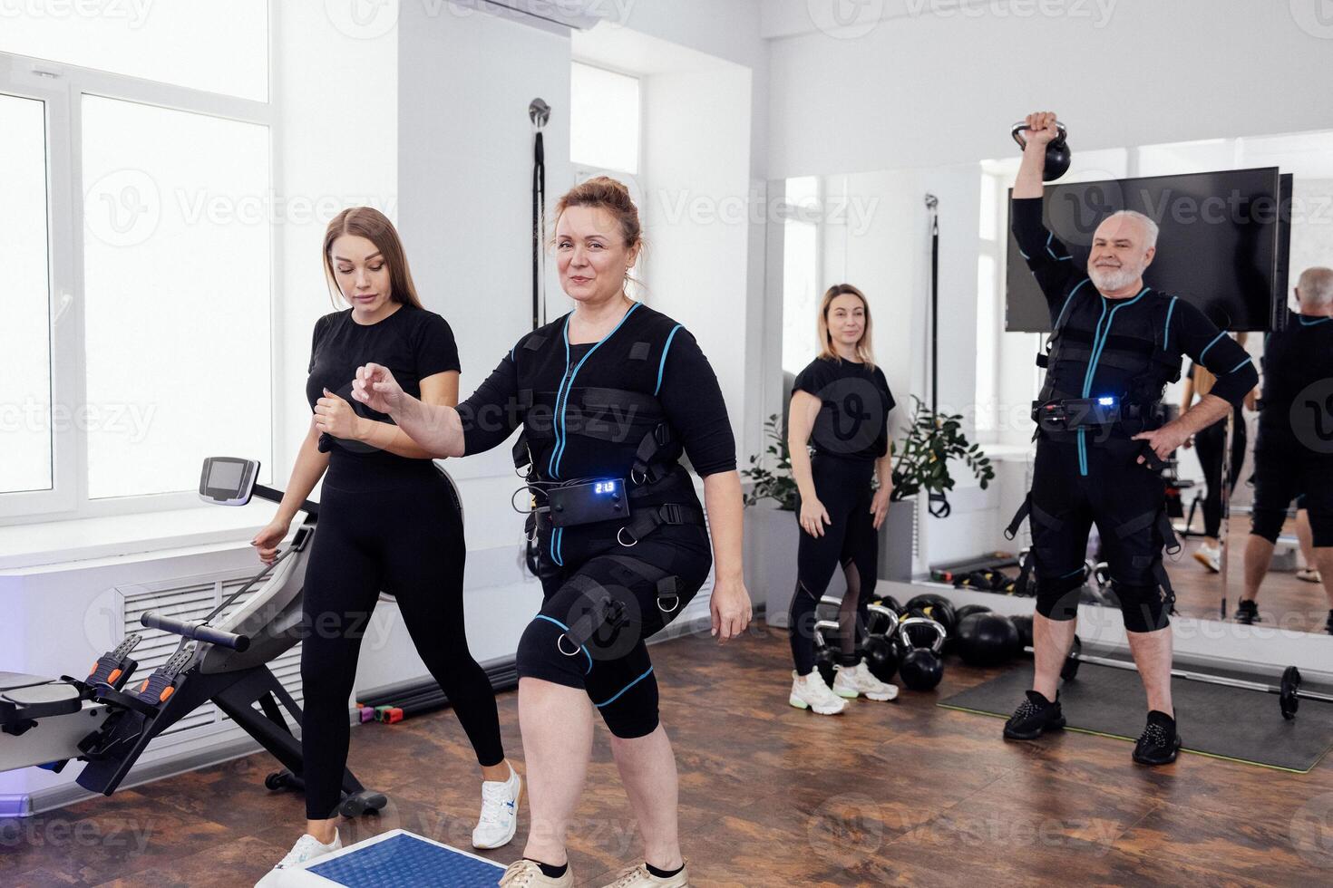 Elderly man doing exercises with kettlebell under guidance of personal trainer. Plump woman middle age is engaged on step platform with her fit coach. photo
