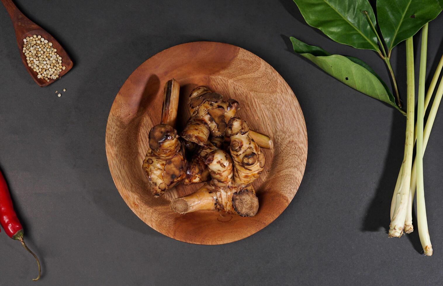 Top view of fresh galangal root on wooden bowl isolated on black background. Galangal root are used in tradtional asian cuisines. photo