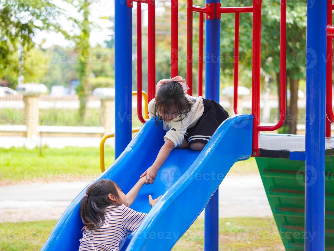 Cute sisters having fun on a colorful slide in an outdoor park. Children playing in the playground during summer vacation. photo