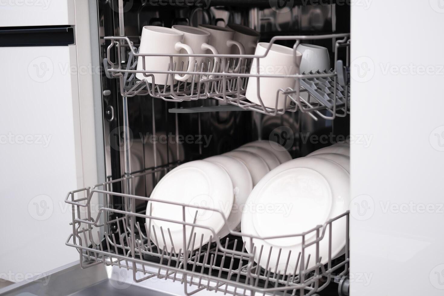 Built-in dishwasher door open, close-up of white plates and mugs photo