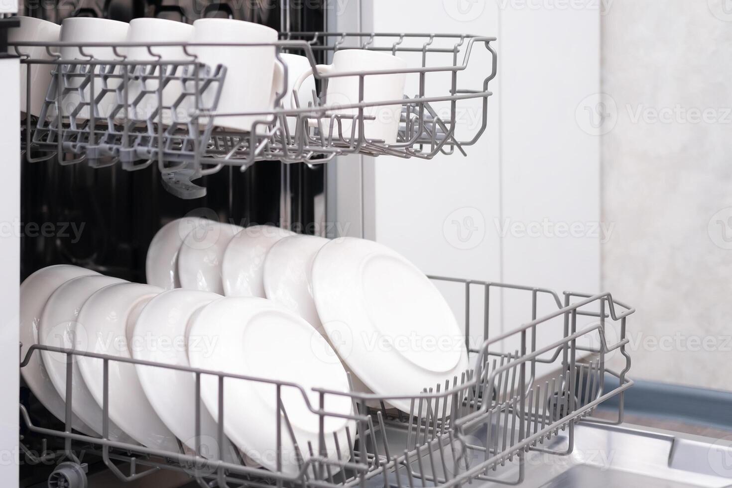 The door of the built-in dishwasher is open, close-up of white mugs photo