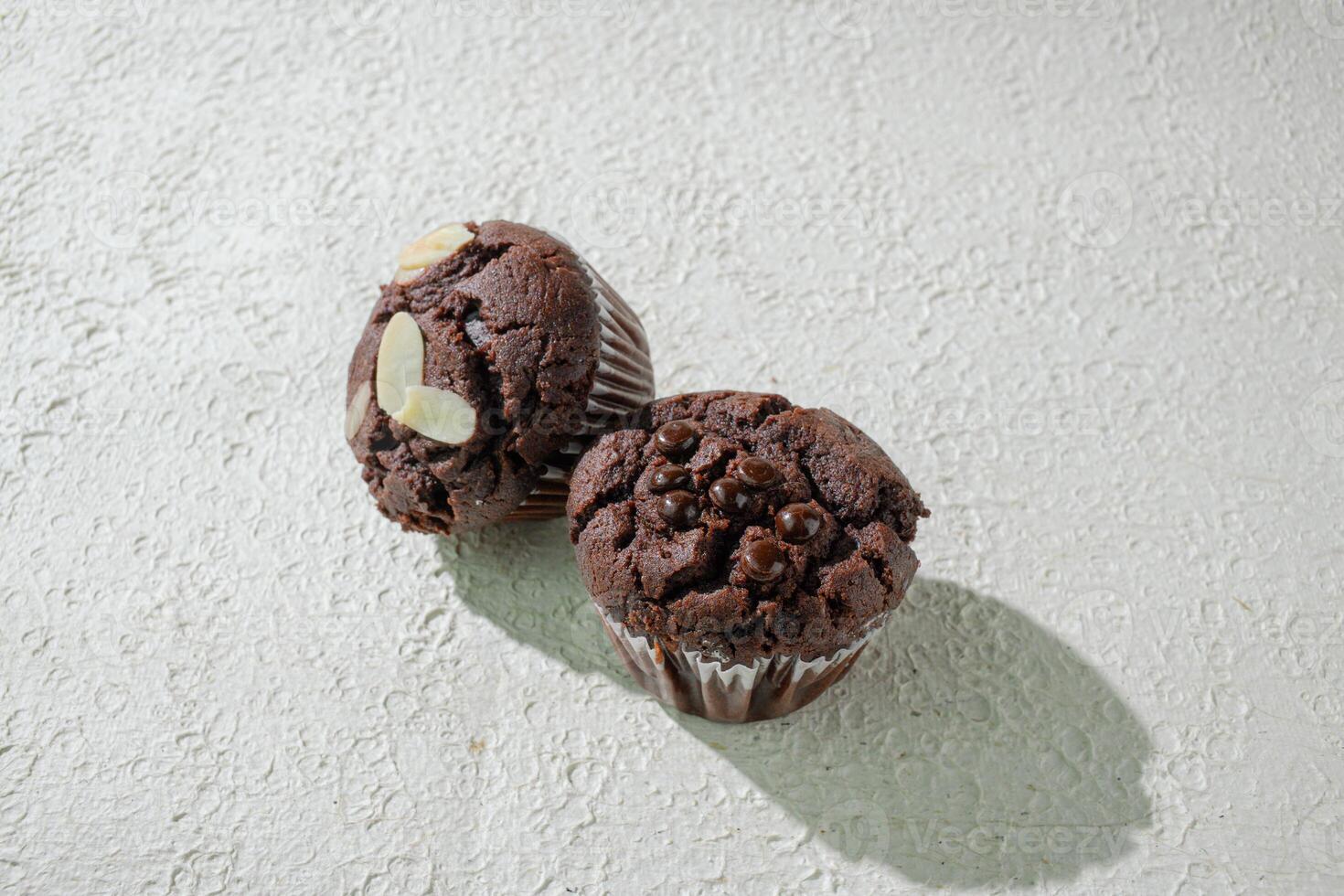 two chocolate muffins sitting on a white texture background photo
