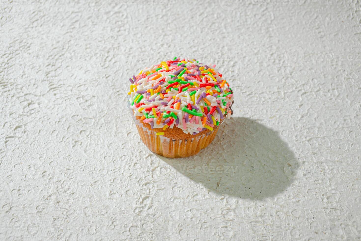 a cupcake with sprinkles on top of a white surface background photo