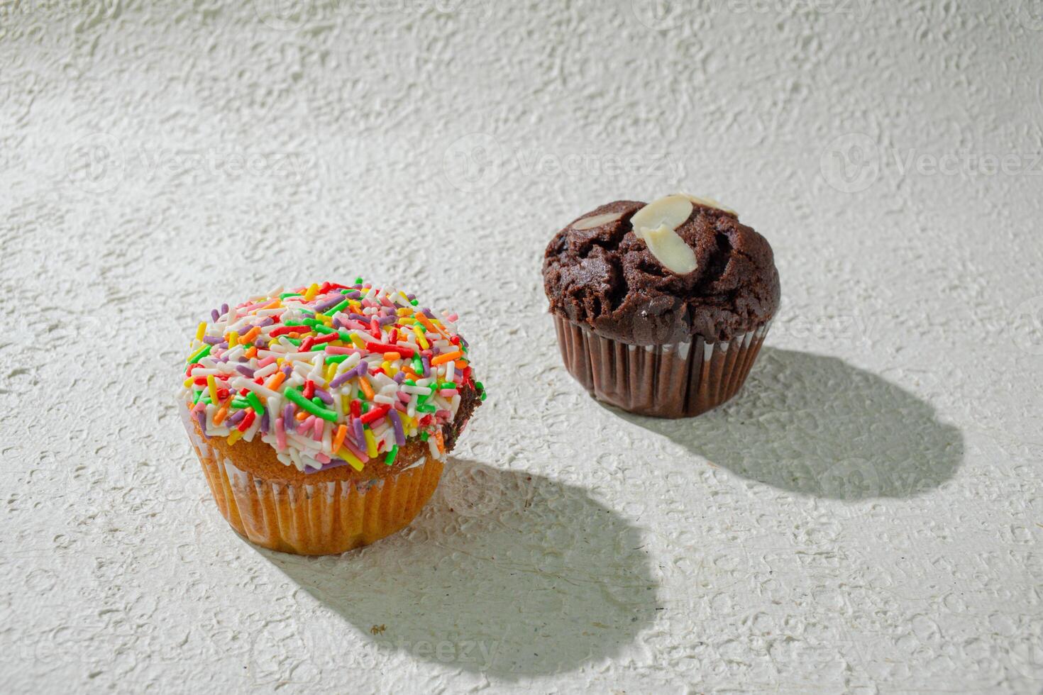 two cupcakes with sprinkles on top of a white surface photo