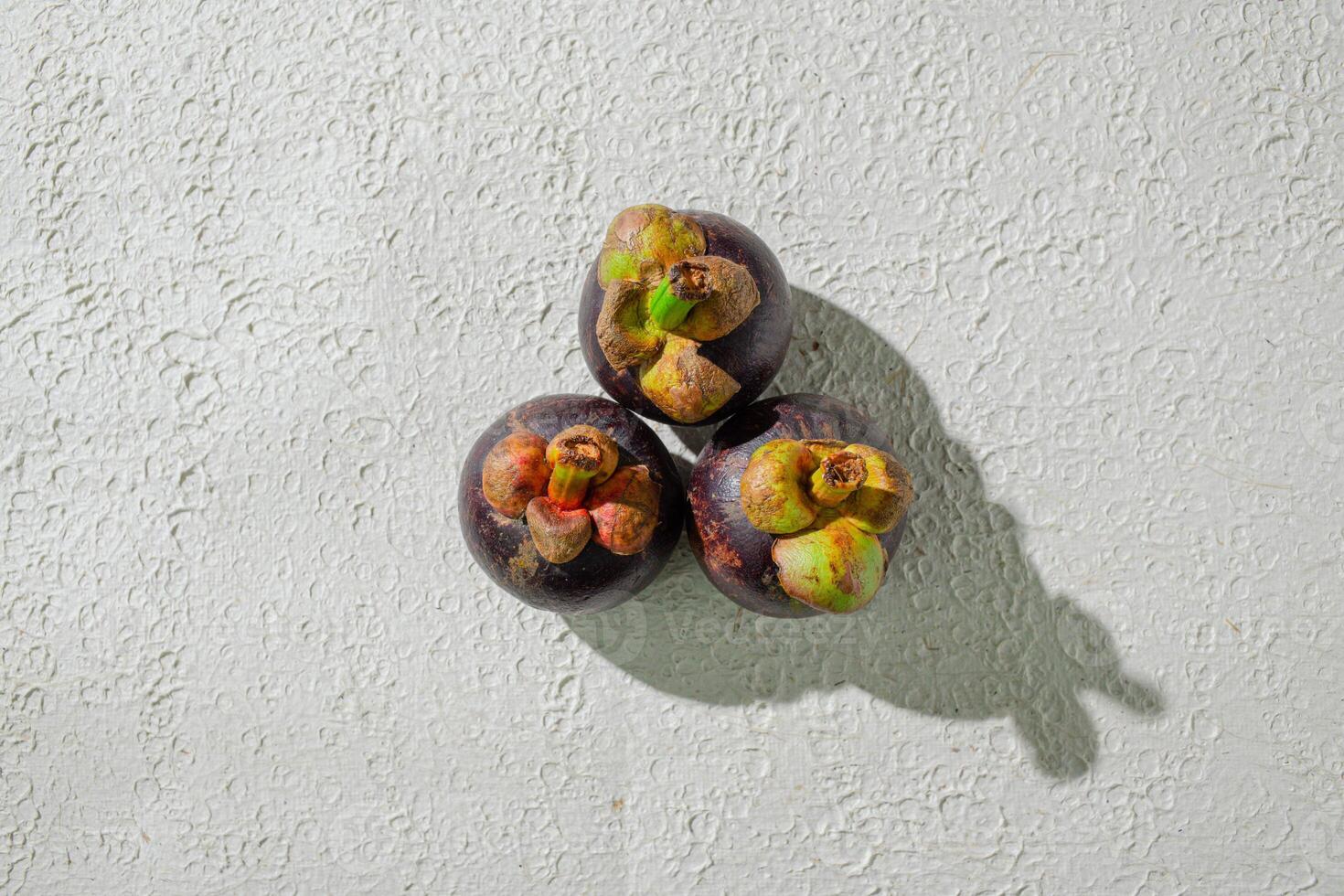 Mangosteen fruit displayed against a textured white background, emphasizing its unique purple rind and freshness. perfect for digital asset photo