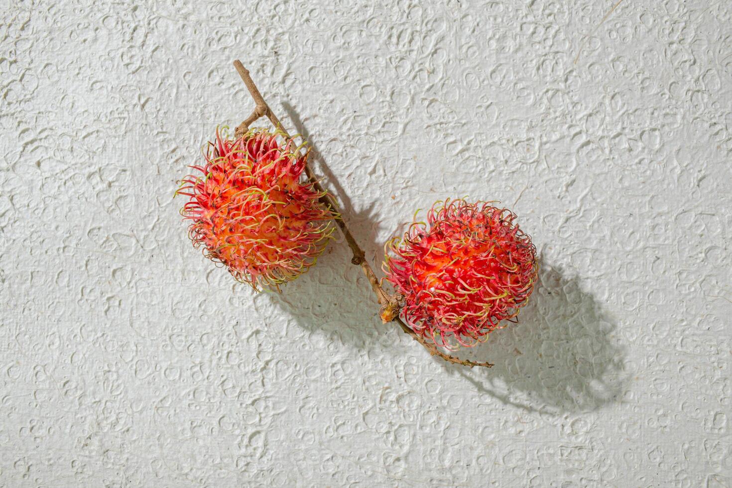 Fresh two red rambutan on a textured white background, perfect as a digital asset for design projects, posters, advertisements, or creative media photo