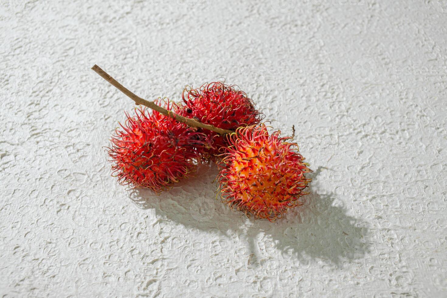 Fresh three red red rambutan fruit on a textured white background, perfect as a digital asset for design projects, posters, advertisements, or creative media photo