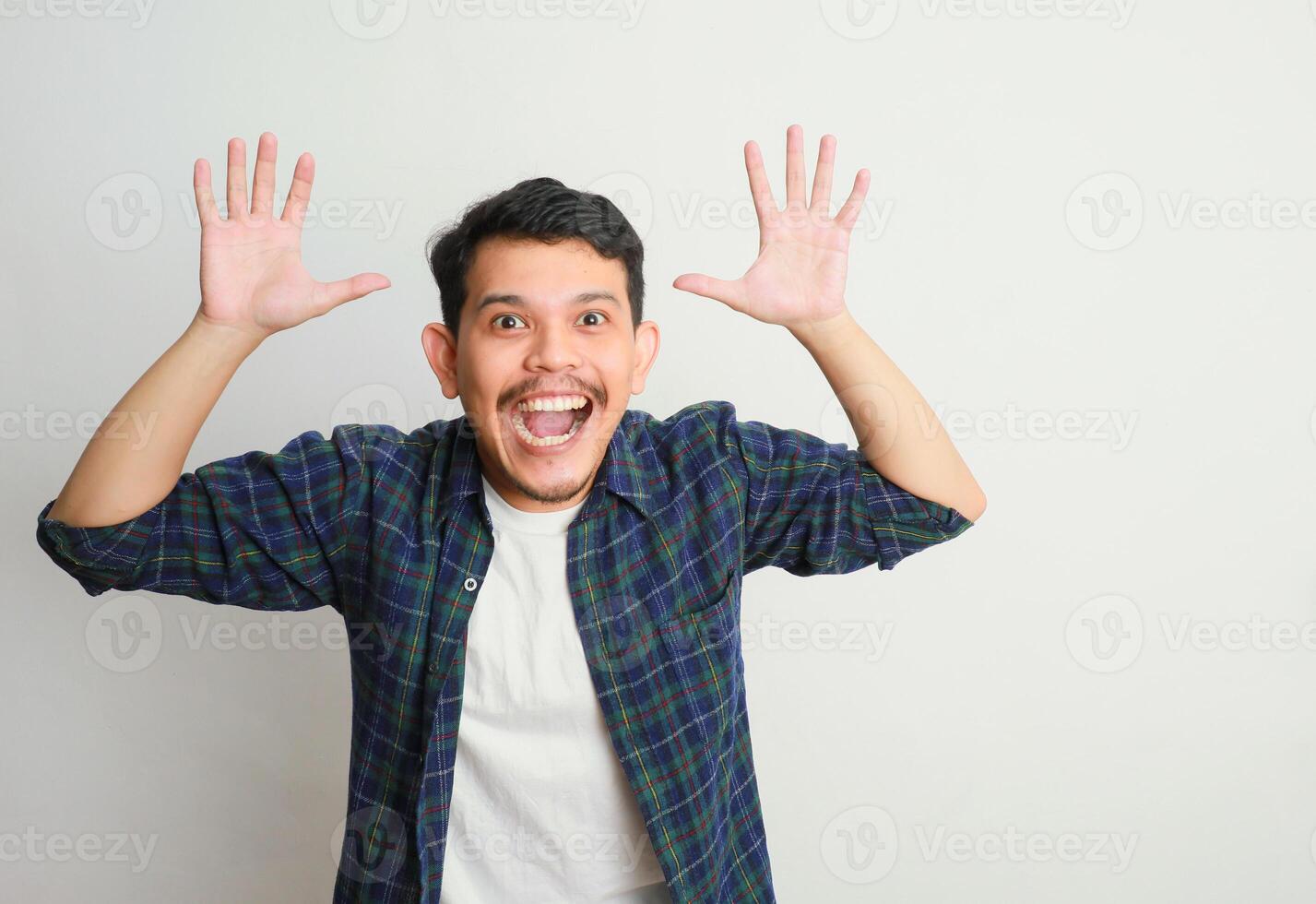 an Excited handsome young Asian man looking up with a happy expression while raising arms isolated on white background photo