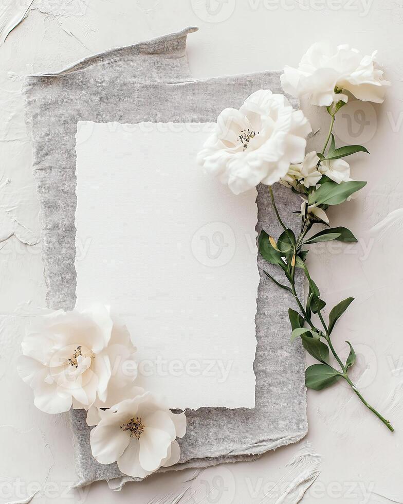 Creative flat lay composition with delicate white flowers arranged around blank card on white background, invitation photo