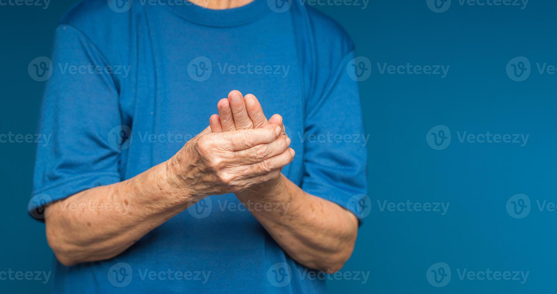 Senior woman suffering from hand pain while standing on a blue background photo