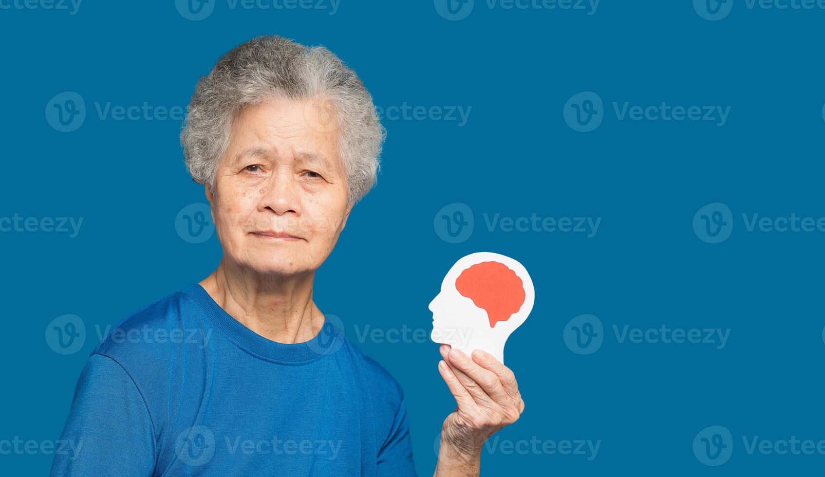 Portrait of a senior woman holding a brain symbol while standing on a blue background photo