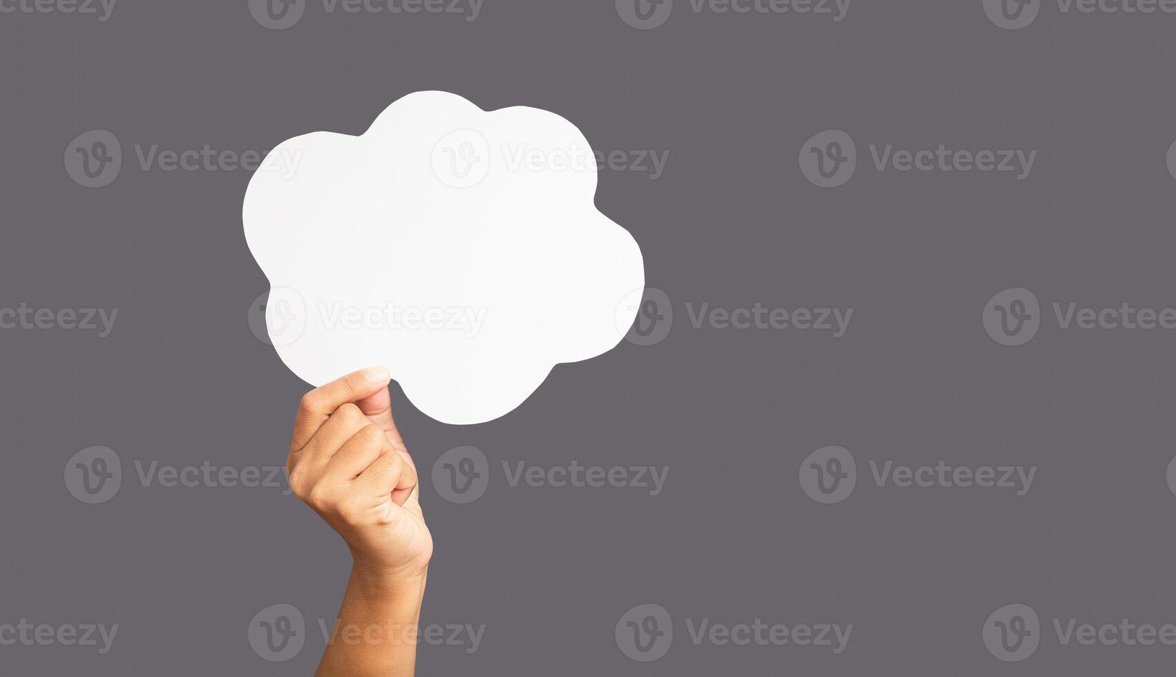 Close-up of hand holding a white speech bubble cloud against a gray background photo