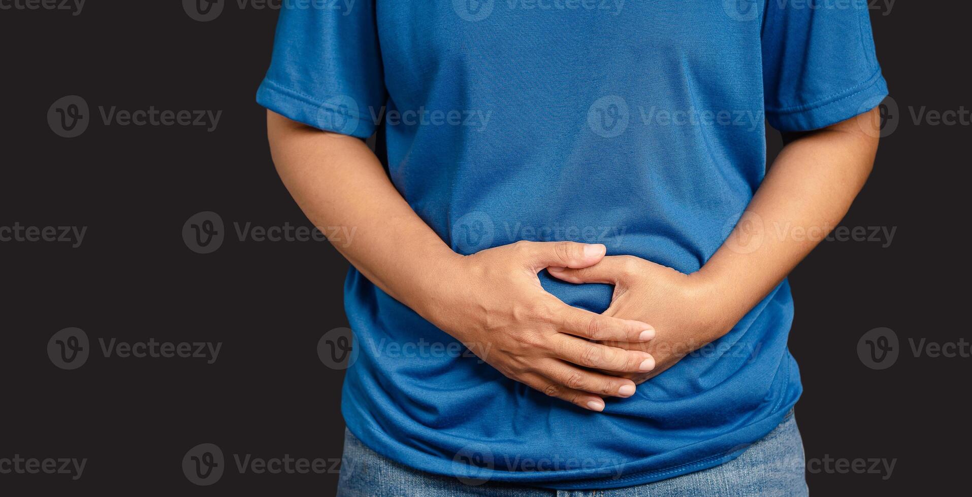 A young woman suffering from abdominal pain used her hand to hold her belly while standing on a gray background photo