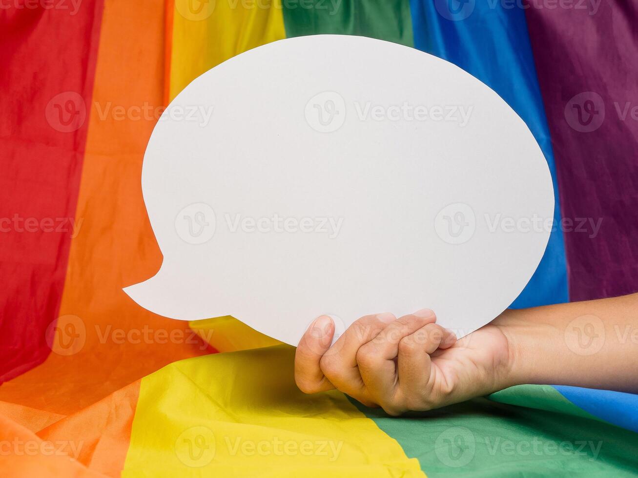 Hand holding a white speech bubble on the rainbow flag or LGBT flag background photo