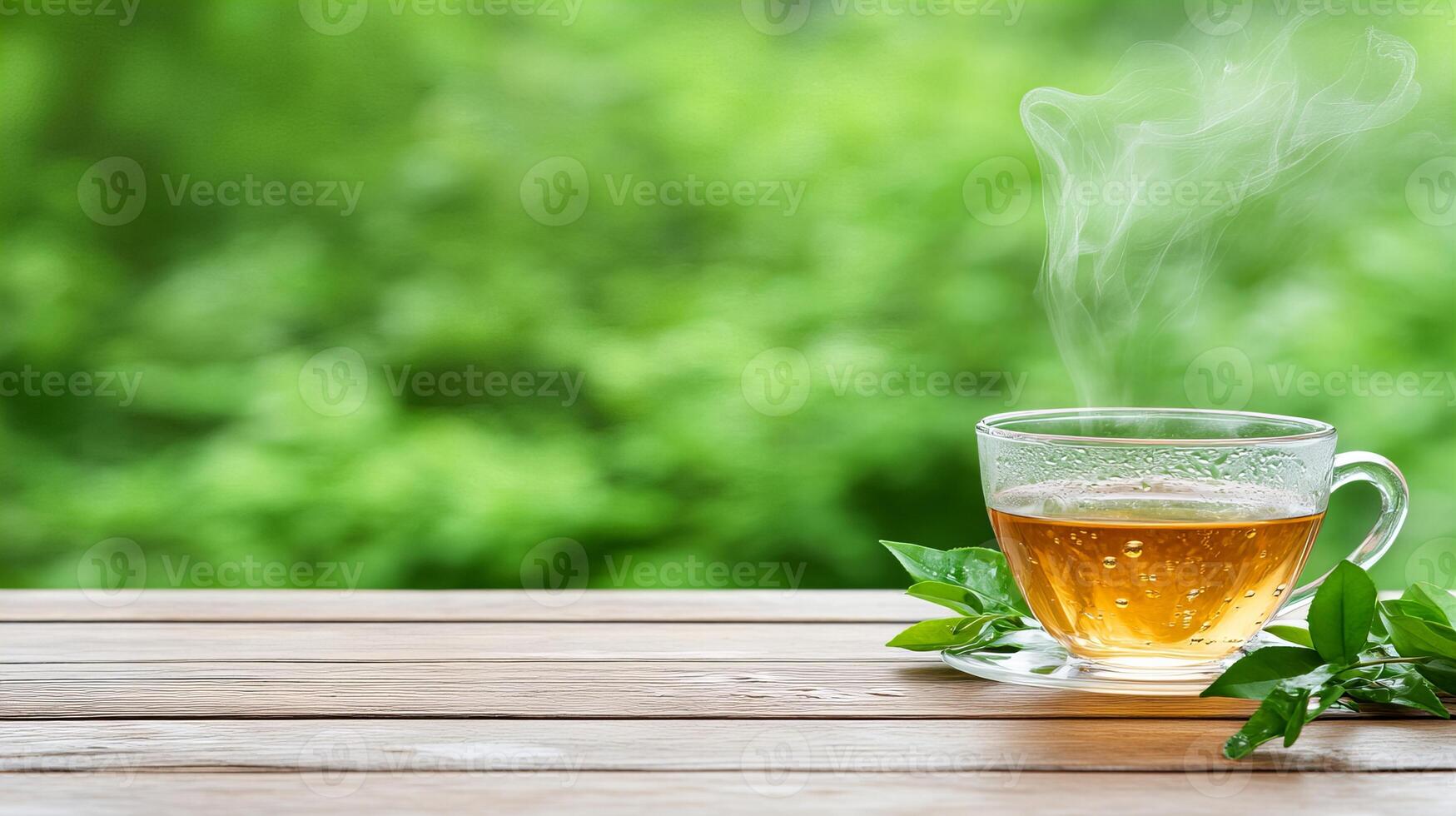 Steaming green tea in a glass cup on a wooden table with leafy green background photo