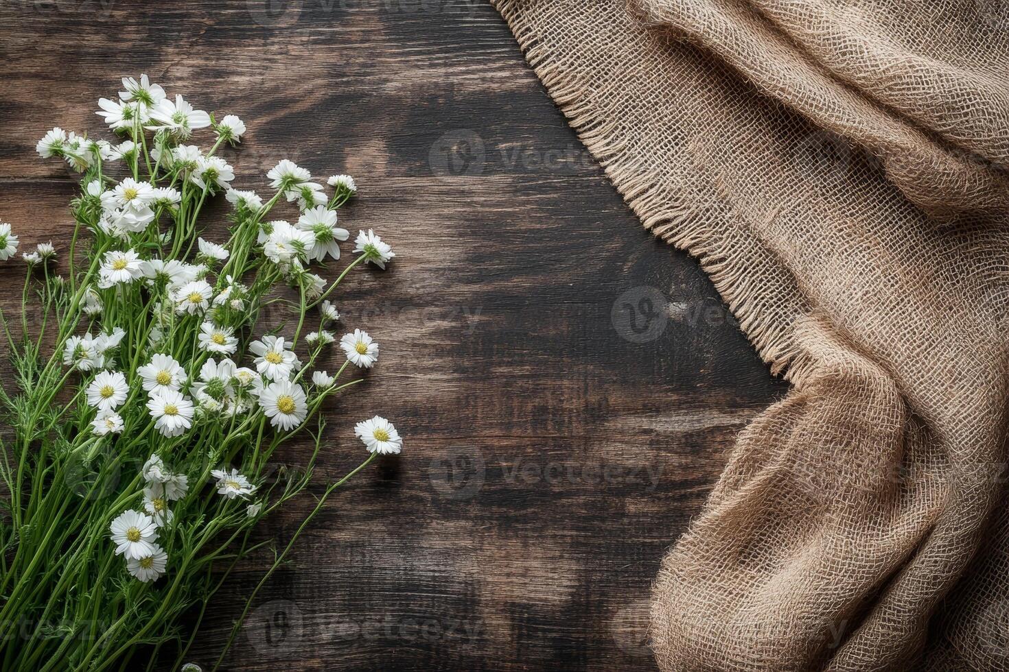 A rustic arrangement of white flowers beside a burlap cloth on a wooden surface. photo