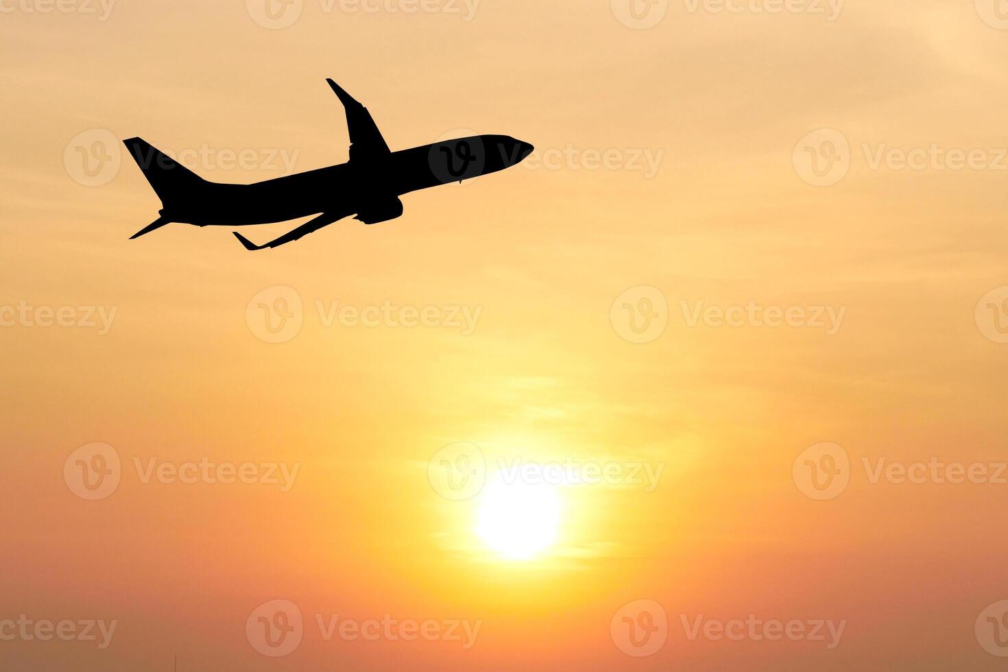 Silhouette of Airplane Soaring Against a Vibrant Orange Sunset Sky with Glowing Sun on the Horizon photo