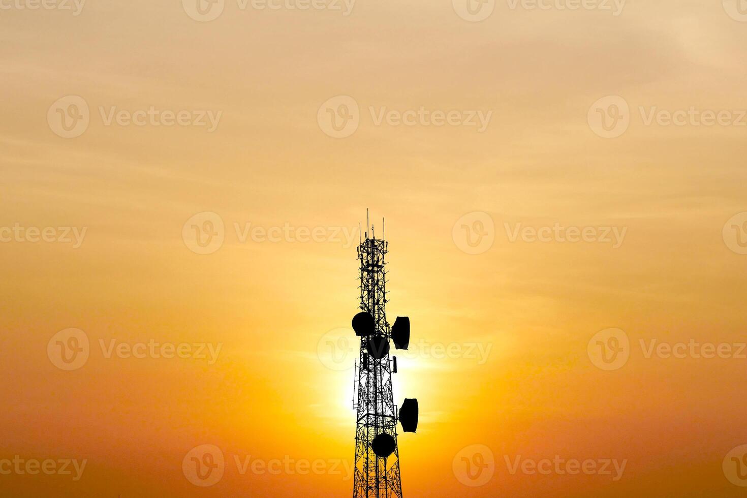 Silhouette of a Communication Tower Against a Vibrant Sunset Sky with Orange and Yellow Hues photo