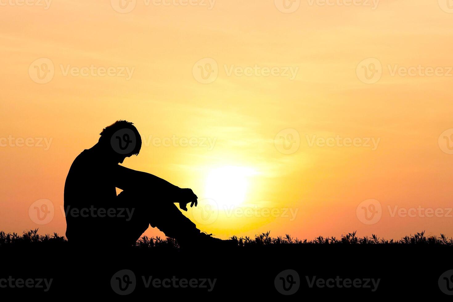 Silhouette of a Person Sitting Thoughtfully Against a Vibrant Sunset Sky in a Tranquil Outdoor Setting photo