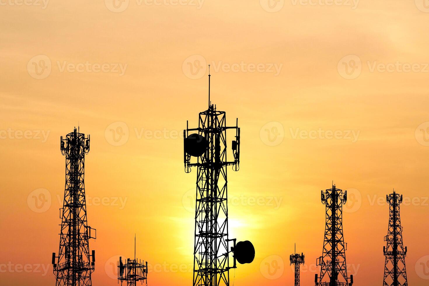 Silhouetted Communication Towers Against a Vibrant Sunset Sky with Orange and Yellow Hues photo