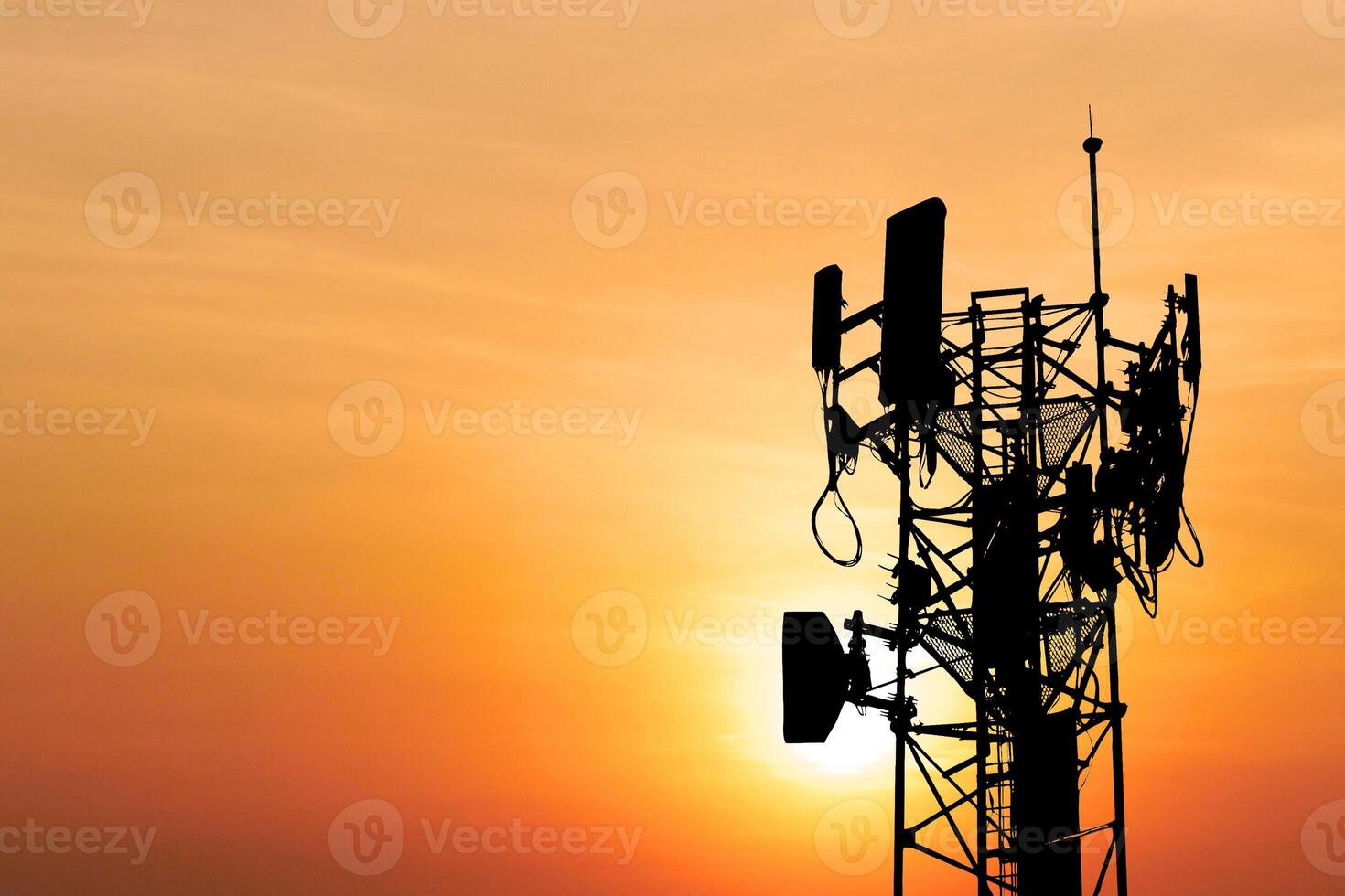 Silhouette of a Communication Tower Against a Vibrant Orange Sunset Sky with Antennas and Cables in a Scenic Evening Landscape photo