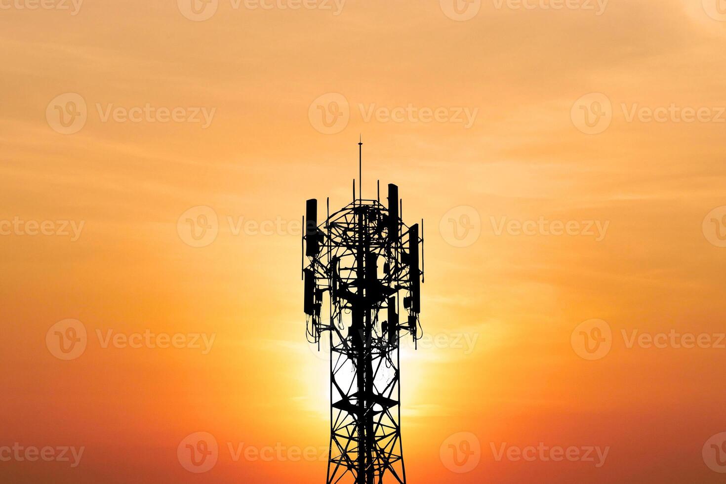 Silhouette of a Communication Tower Against a Vibrant Orange Sunset Sky with Radiant Sunlight in the Background photo