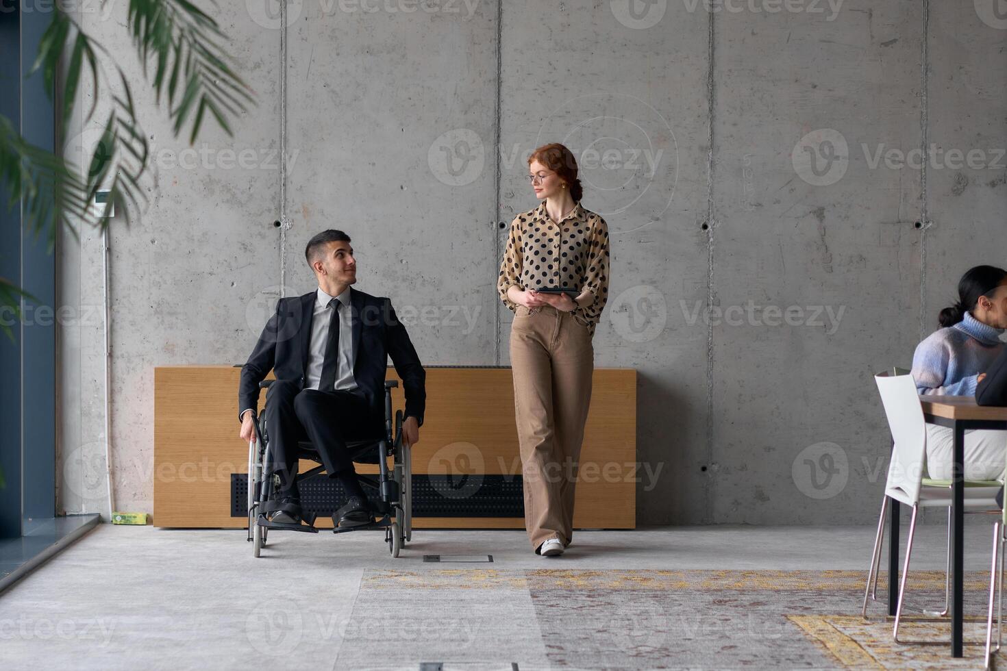 Director in a Wheelchair Engaging in a Business Discussion with a Colleague While Navigating a Modern Office photo