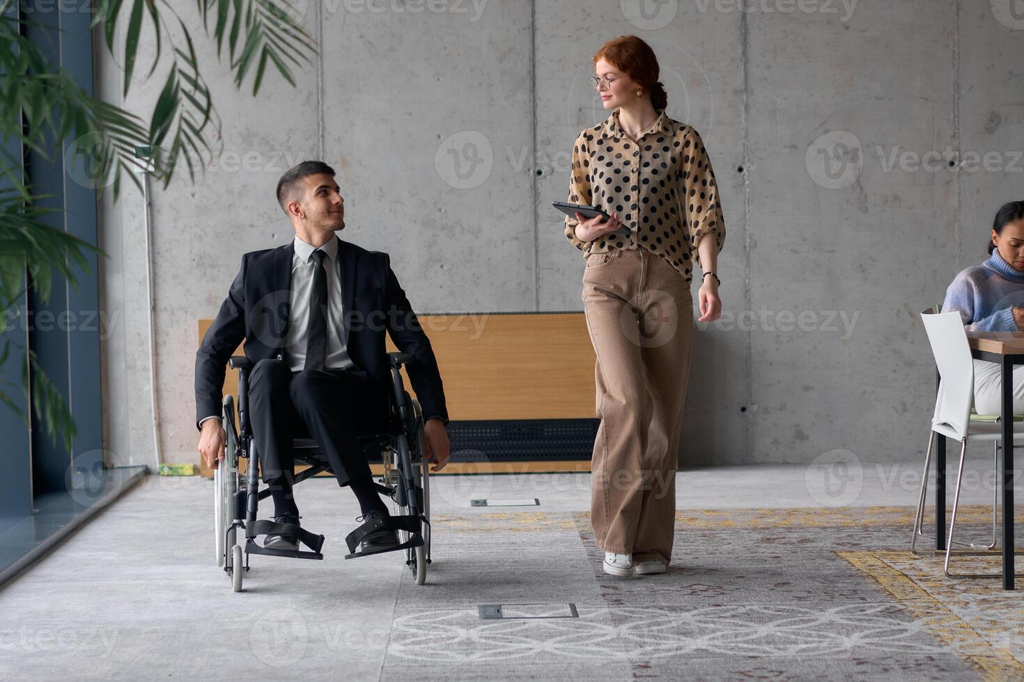 Director in a Wheelchair Engaging in a Business Discussion with a Colleague While Navigating a Modern Office photo