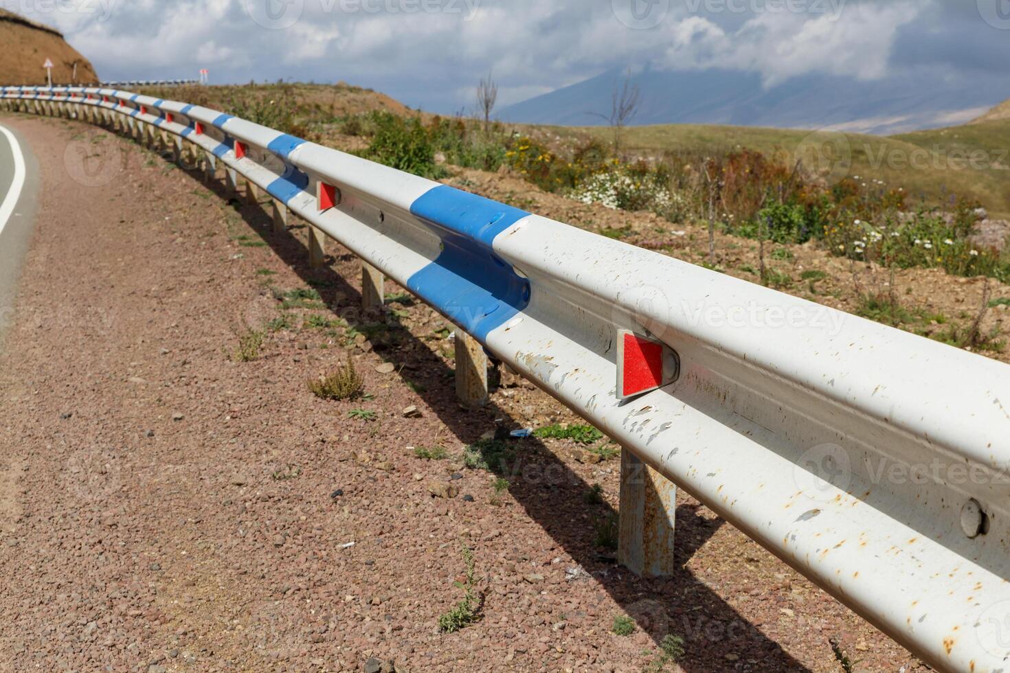 Road safety barriers and winding road in Armenia on a sunny day with clouds photo