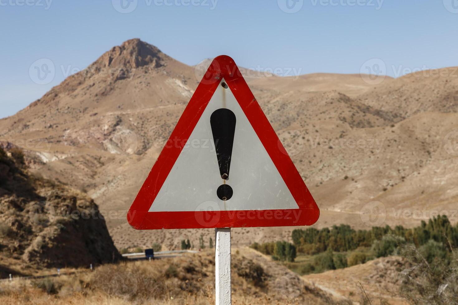 Caution sign alerts drivers in a mountainous area with dry landscape and clear sky photo