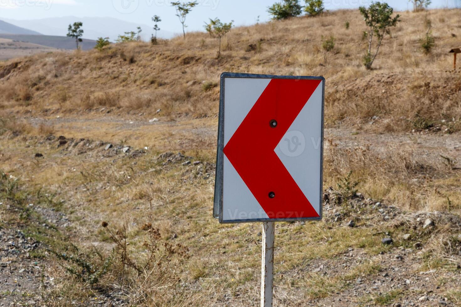 Road sign indicating a sharp turn along a rural pathway in a dry landscape photo