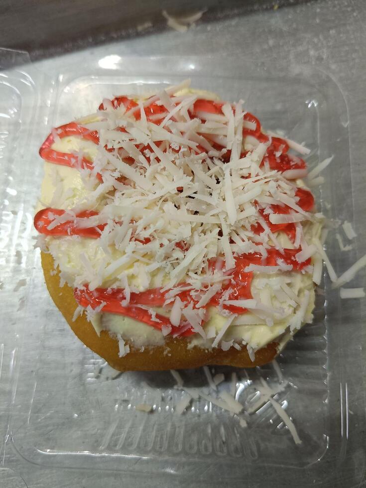 Closeup of a fried donut topped with butter, shaved cheese and strawberry jam photo