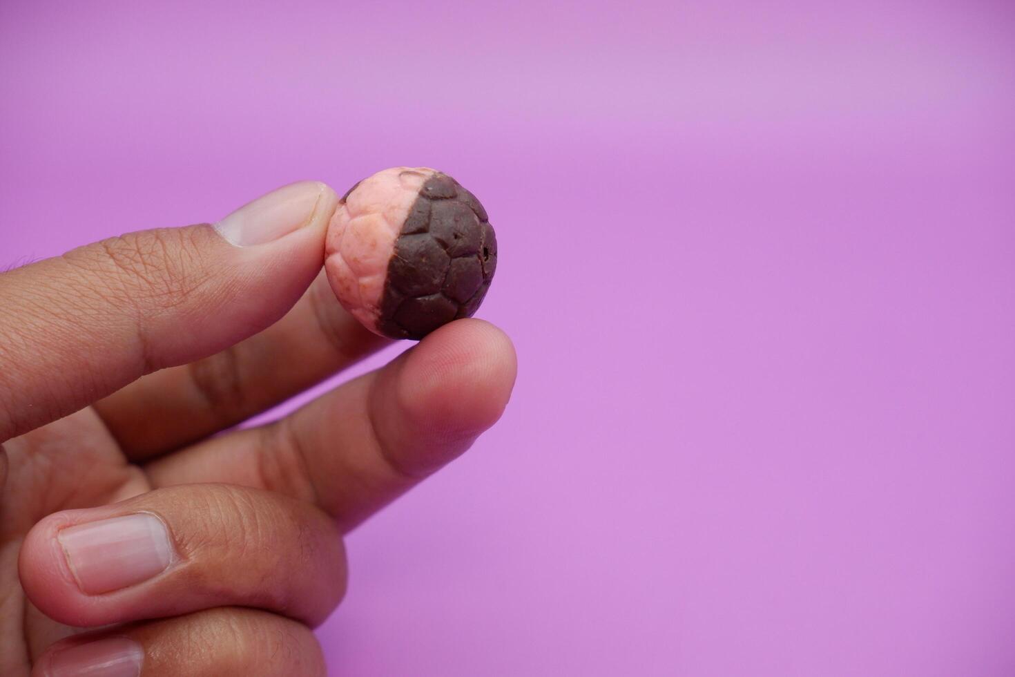 Chocolate ball snack with soccer ball design, hand holding half pink, half brown treat on purple photo