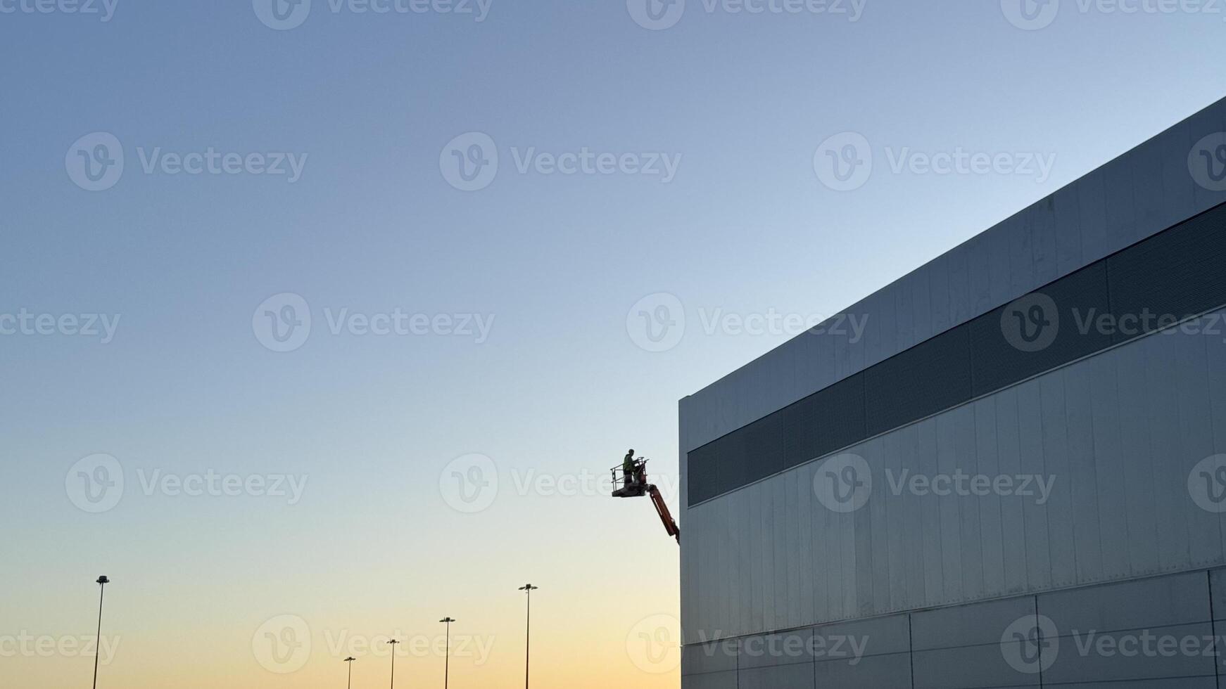 Worker on Lift Maintaining Exterior of Modern Building at Dusk photo
