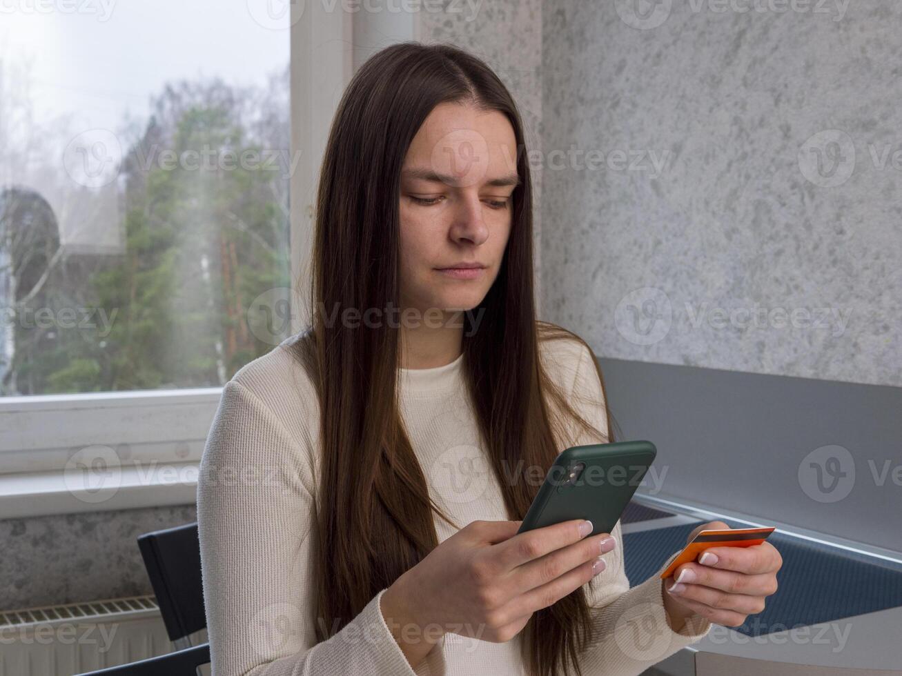Female customer smiling while browsing online store, holding credit card and smartphone, completing digital purchase from comfortable home setting photo