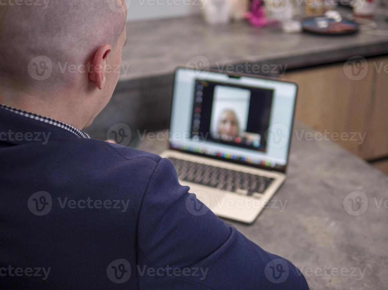 Businessman working from home using laptop for conference with female colleague, discussing business strategies in modern kitchen. Laptop enables seamless remote communication photo