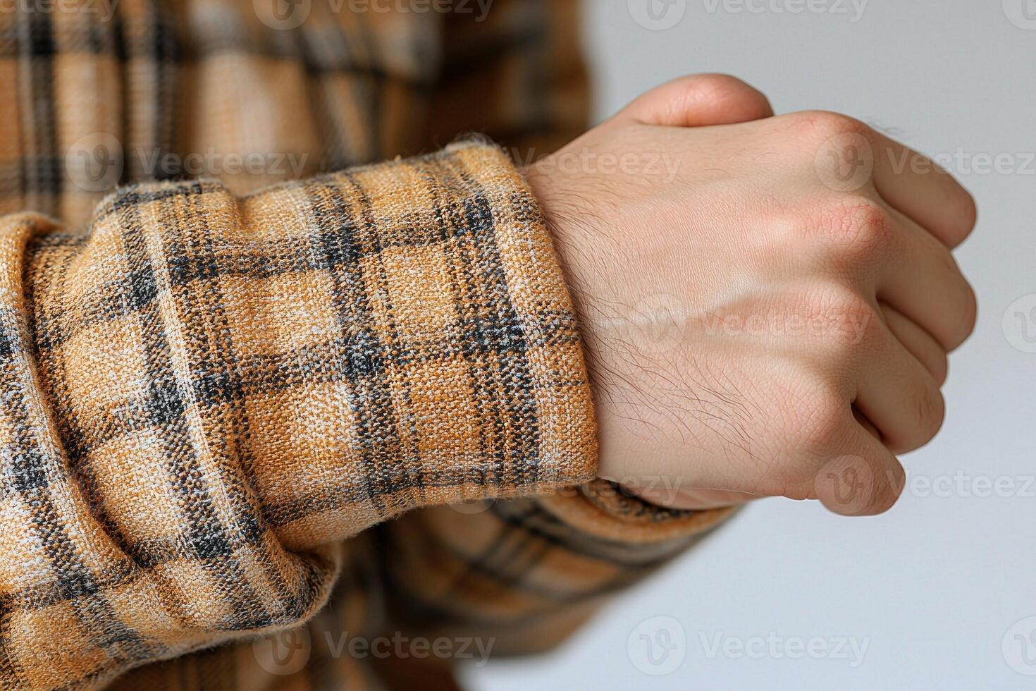 man holds his wrist pained expression while wearing plaid shirt. focus hand and wrist area white backdrop highlighting discomfort associated wrist strain photo