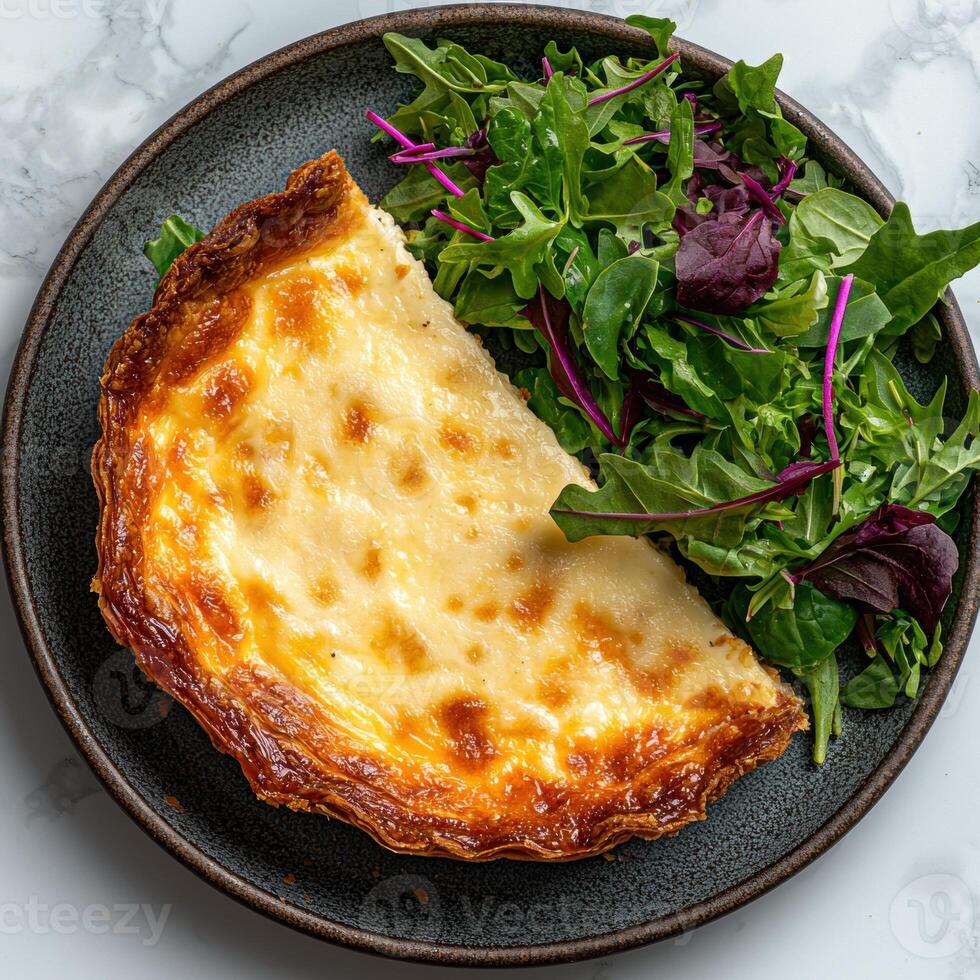 A slice of creamy quiche with a side salad on a dark plate photo