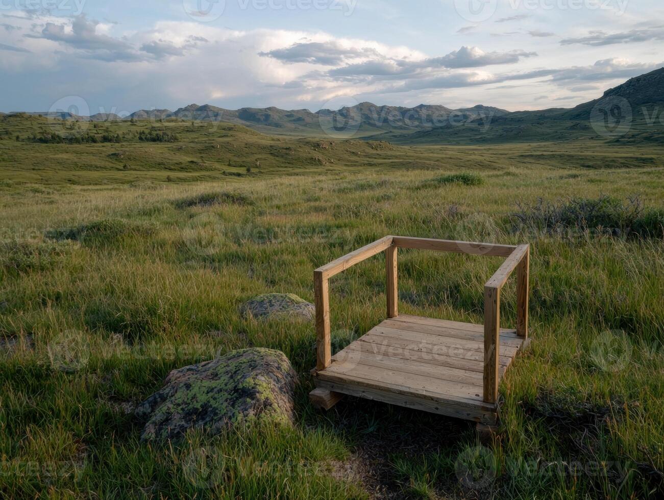 Wooden platform overlooking a vast grassy plain and distant mountains under a partly cloudy sky photo
