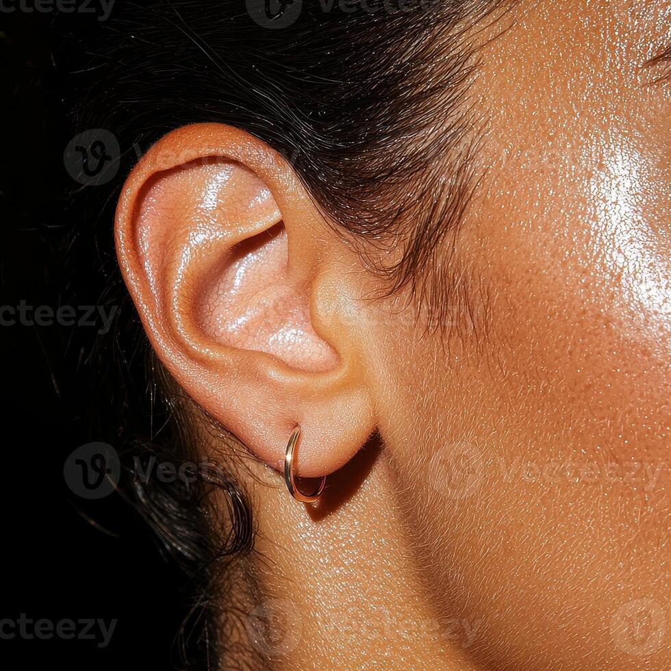 Close up of a womans ear with a small gold hoop earring photo