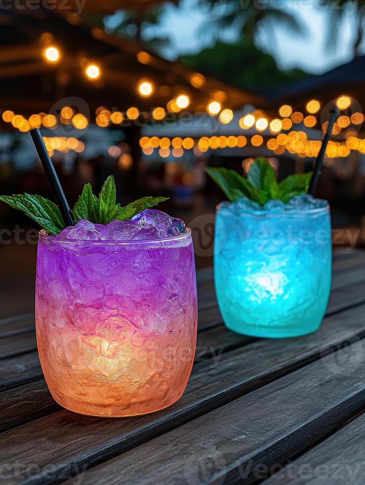 Two colorful cocktails with ice and mint garnish on a wooden table at night photo