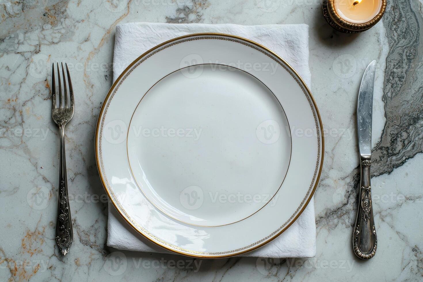 Elegant place setting with gold rimmed plate, silverware, and candle on marble table photo